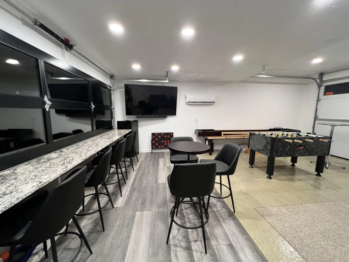 A lively indoor game room featuring a granite bar counter, foosball table, pool table, and television. The space exudes energy and fun, designed for group activities and entertainment well into the evening.